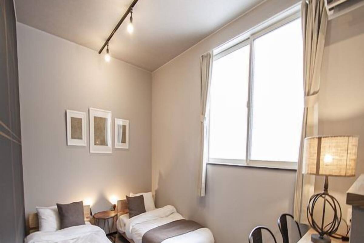 A bedroom with two beds, a desk, and a window.