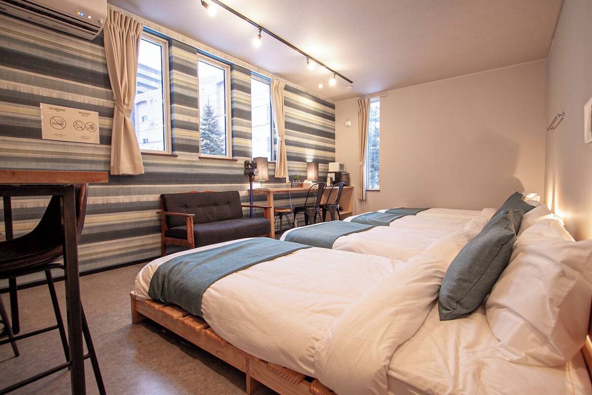 A room with two beds, a desk, a chair, and a window with curtains.