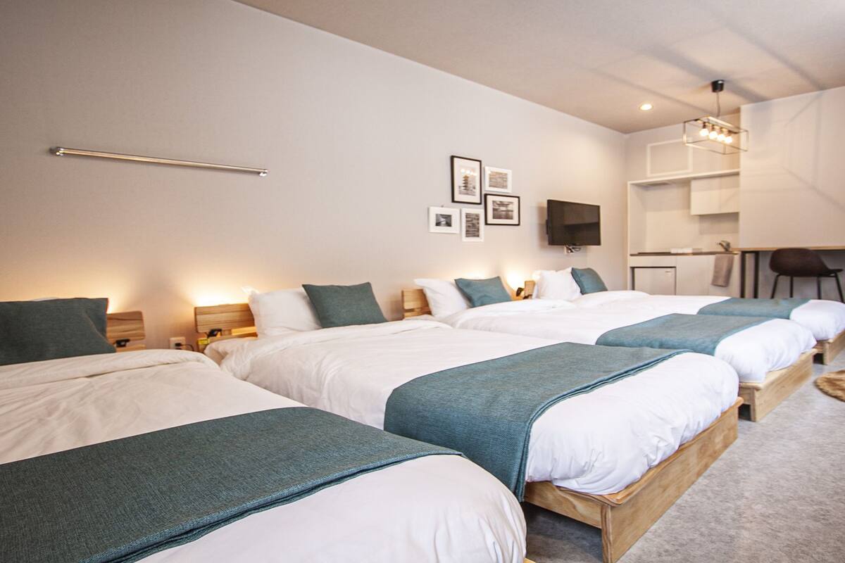 A hotel room with four single beds, a desk, and a chair.
