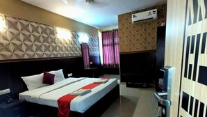 Quarto de hotel com cama, escrivaninha, cadeira, televisão e ar condicionado.
