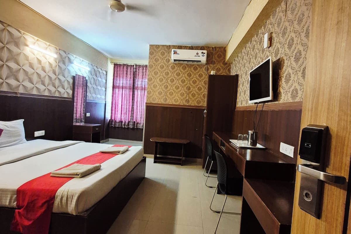 A hotel room with a bed, desk, chair, TV, air conditioning unit, and a ceiling fan.