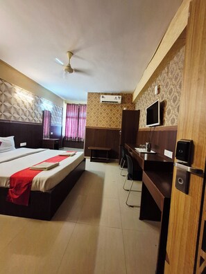 Ein Hotelzimmer mit Bett, Schreibtisch, Stuhl, Fernseher, Klimaanlage und Deckenventilator.