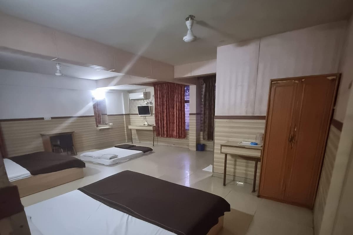 A hotel room with two beds, a desk, a wardrobe, and a bathroom visible through a glass partition.