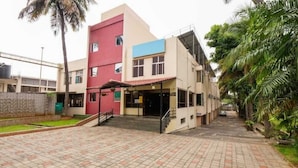 Um edifício de vários andares com fachada vermelha e azul, um pátio com azulejos e palmeiras.