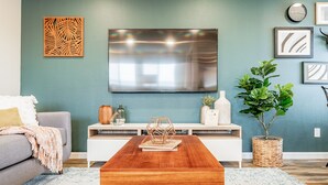 Un salón con una mesa de centro de madera, un sofá gris, un televisor montado en la pared y una planta en maceta.