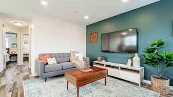 A modern living room with a grey sofa, wooden coffee table, and a large flat-screen TV mounted on a teal wall.