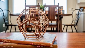 Una escultura metálica geométrica sobre un libro titulado "Australia" en un comedor con sillas y una mesa de madera.