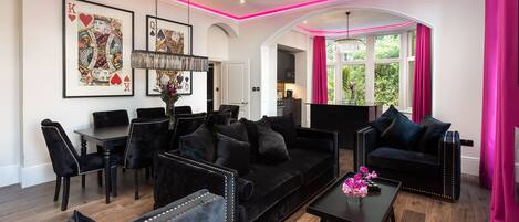 Una sala de estar moderna con muebles negros, un comedor y una cocina visible a través de un arco.