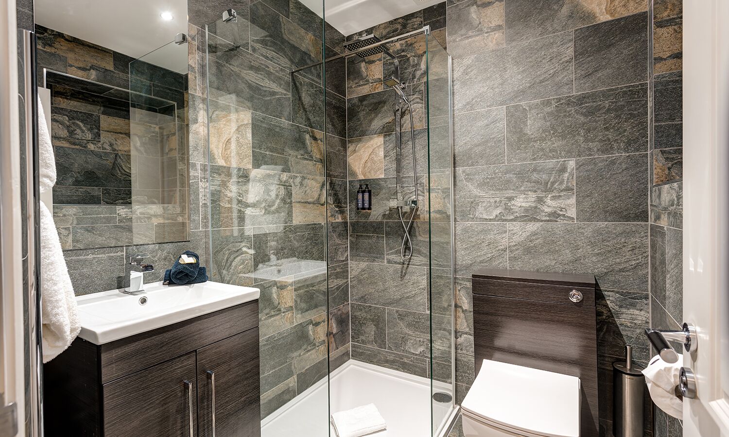 A modern bathroom with a glass-enclosed shower, a white sink, and dark wood cabinetry.