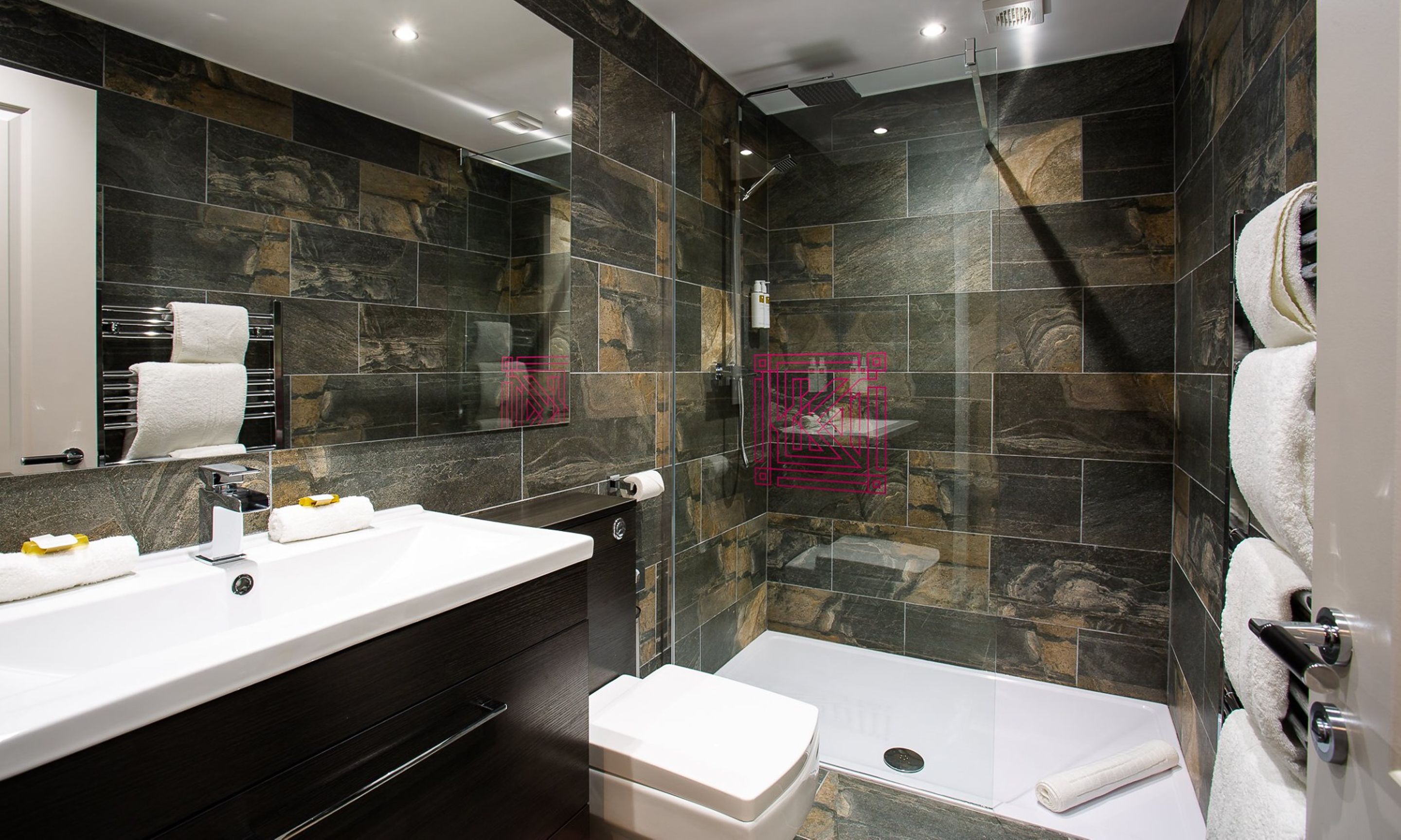 A modern bathroom with a large mirror, a white sink, a dark vanity, a shower enclosure, and a toilet.