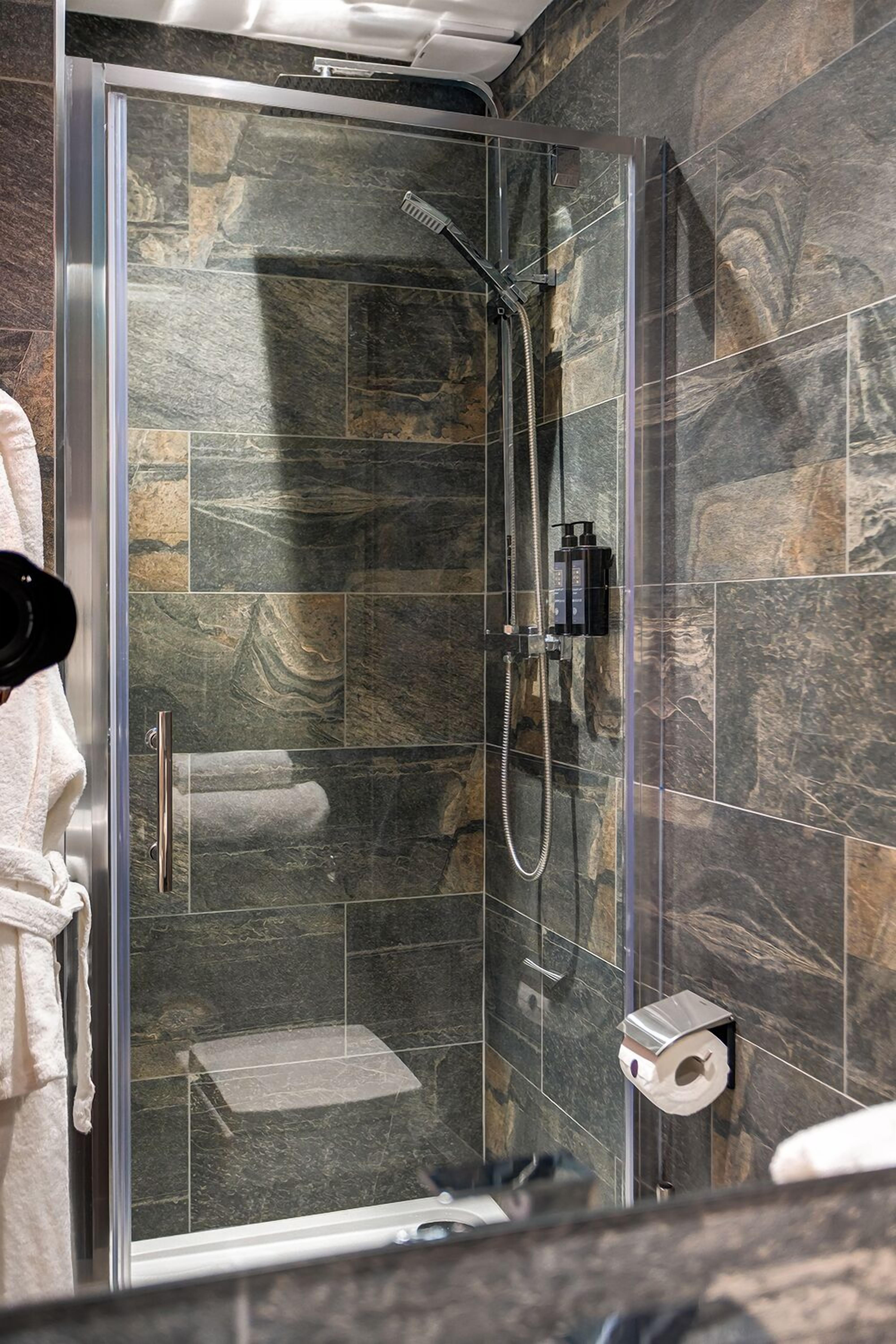 Eine begehbare Duschkabine mit Handbrause, einem Handtuchhalter und einem Toilettenpapierhalter an der Wand.
