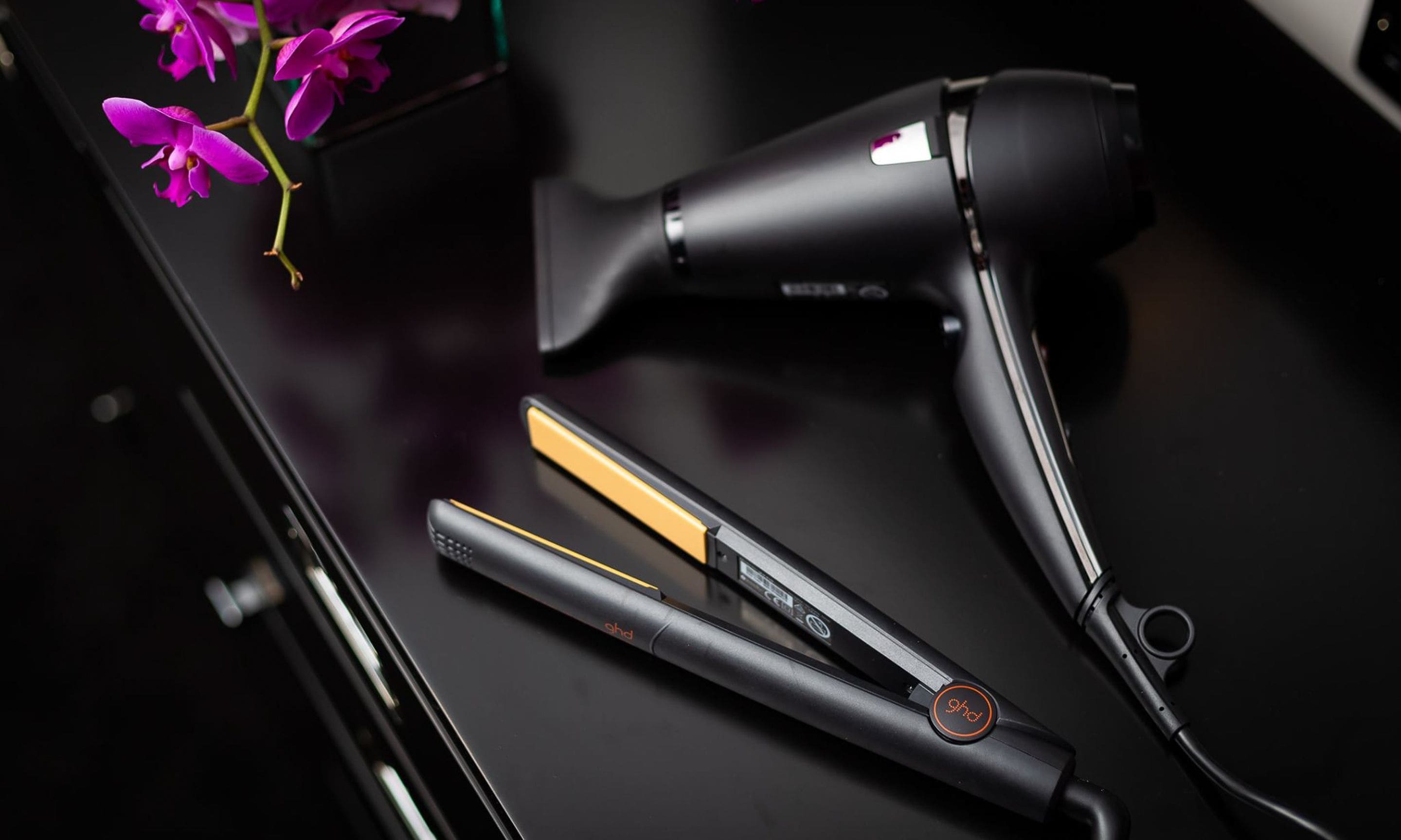 Un lisseur et un sèche-cheveux posés sur une surface noire.