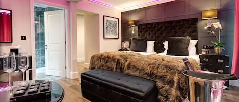 A modern bedroom with a large bed, a glass coffee table, and a minibar.