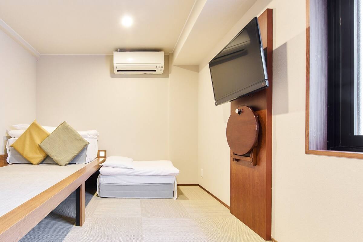 Una habitación pequeña y ordenada, con cama, televisión montada en la pared y equipo de aire acondicionado.