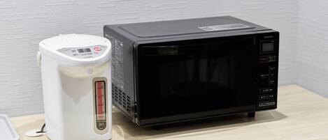 A microwave and a rice cooker on a wooden surface against a white brick wall.