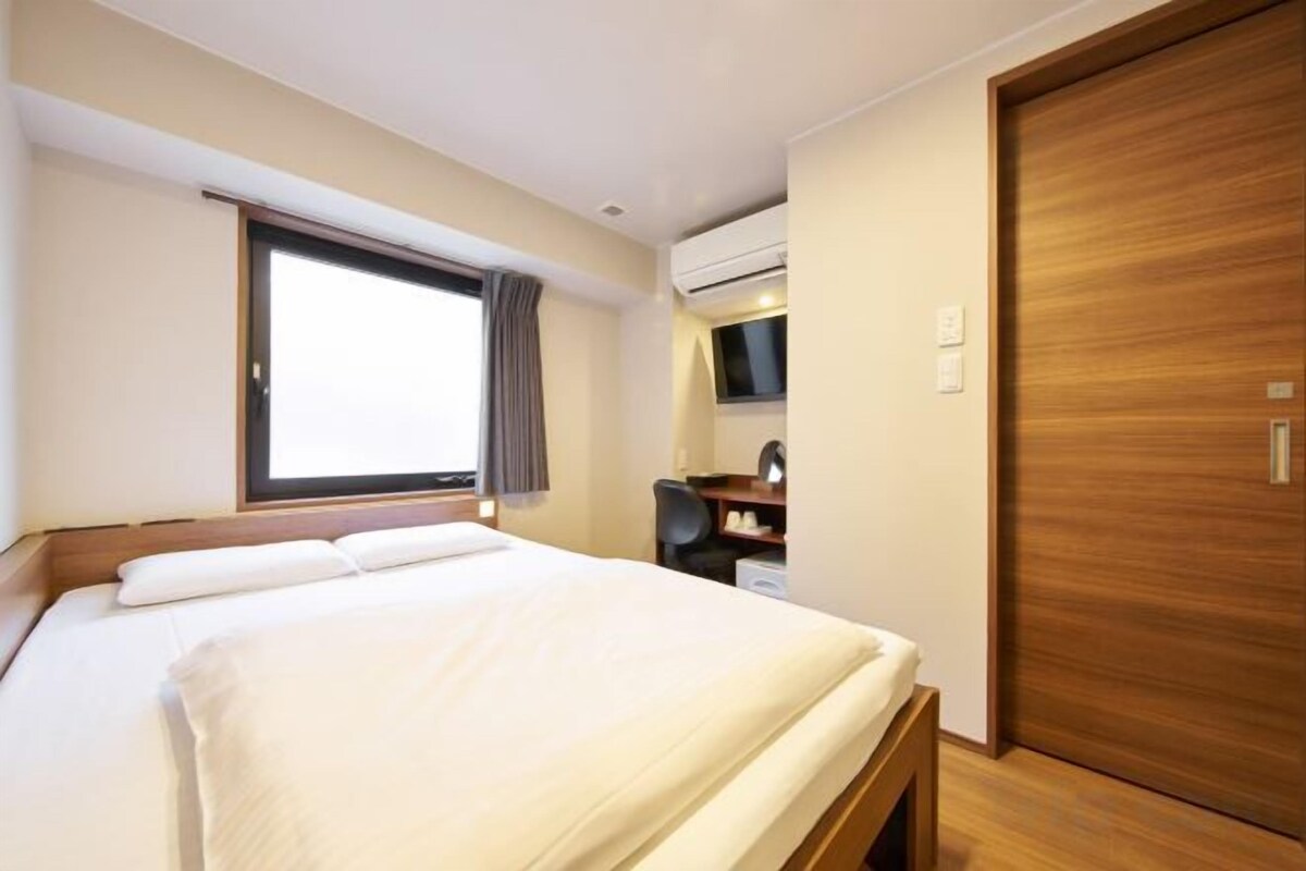 A hotel room with a bed, a desk, a window, and a door.