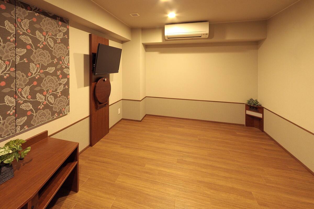 Una habitación con suelo de madera, un televisor de pantalla plana montado en la pared y una planta pequeña sobre una mesita.