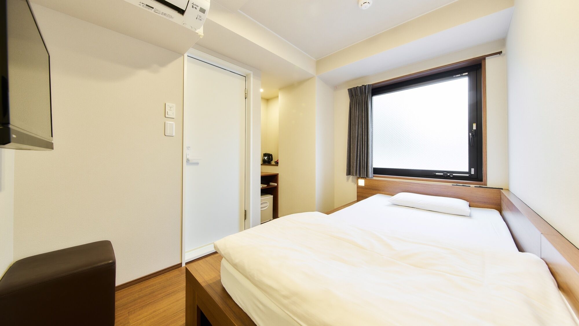 A hotel room with a bed, a desk, a chair, a window with curtains, and a door.