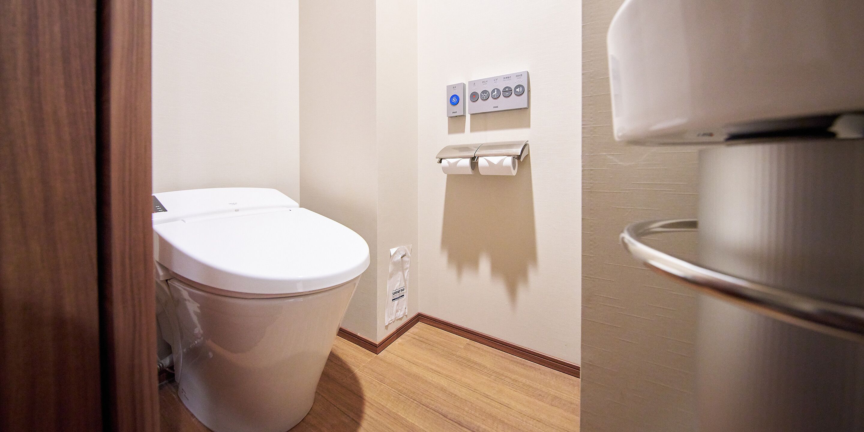 Un baño con un inodoro blanco, dispensador de toallas de papel y secamanos.