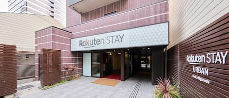 Exterior del Rakuten Stay Urban Osaka Higobashi, con una fachada moderna, una entrada destacada y una alfombra roja que lleva al interior.