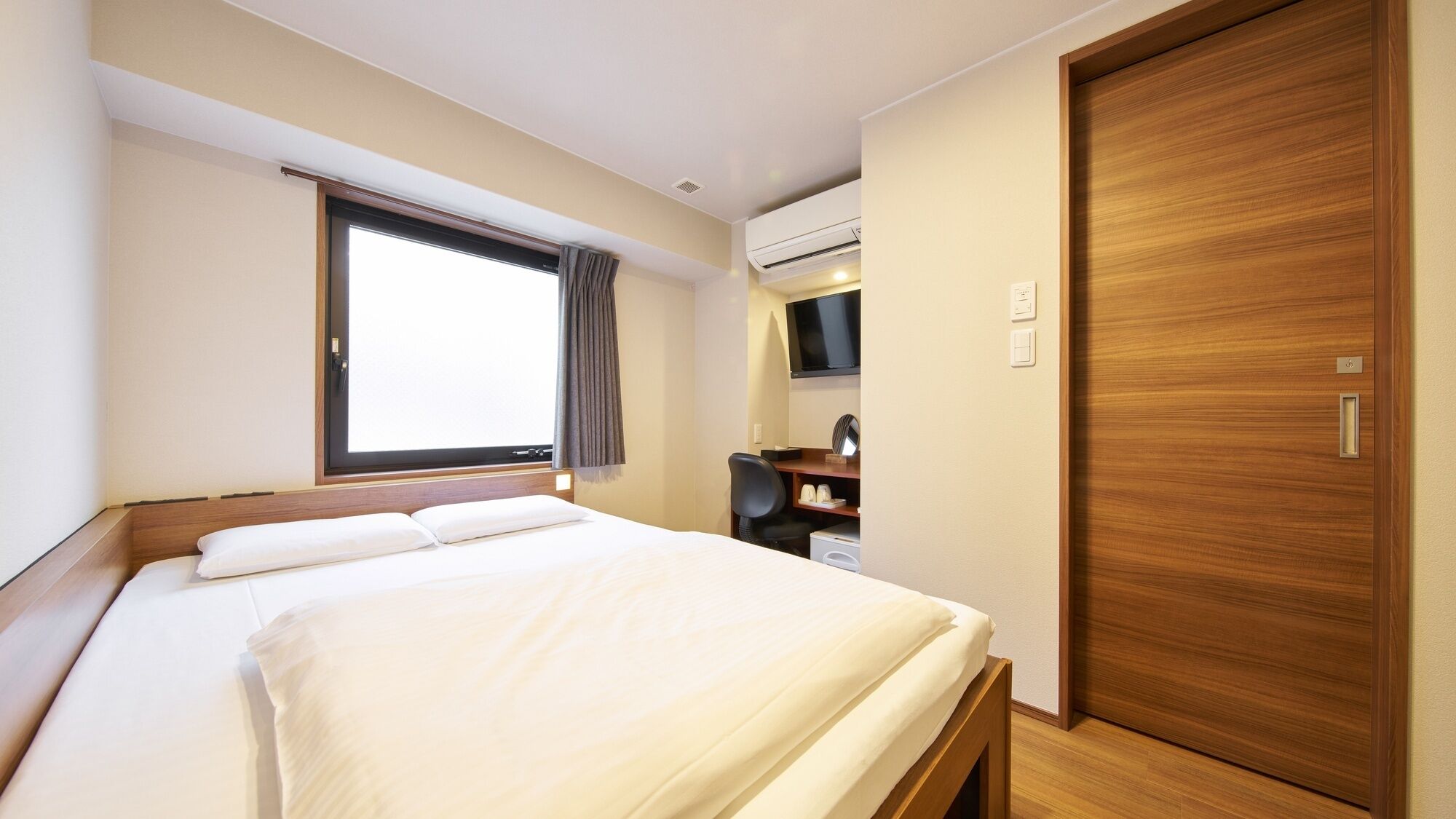 A hotel room with a bed, a desk, a TV, an air conditioning unit, and a wooden wardrobe.