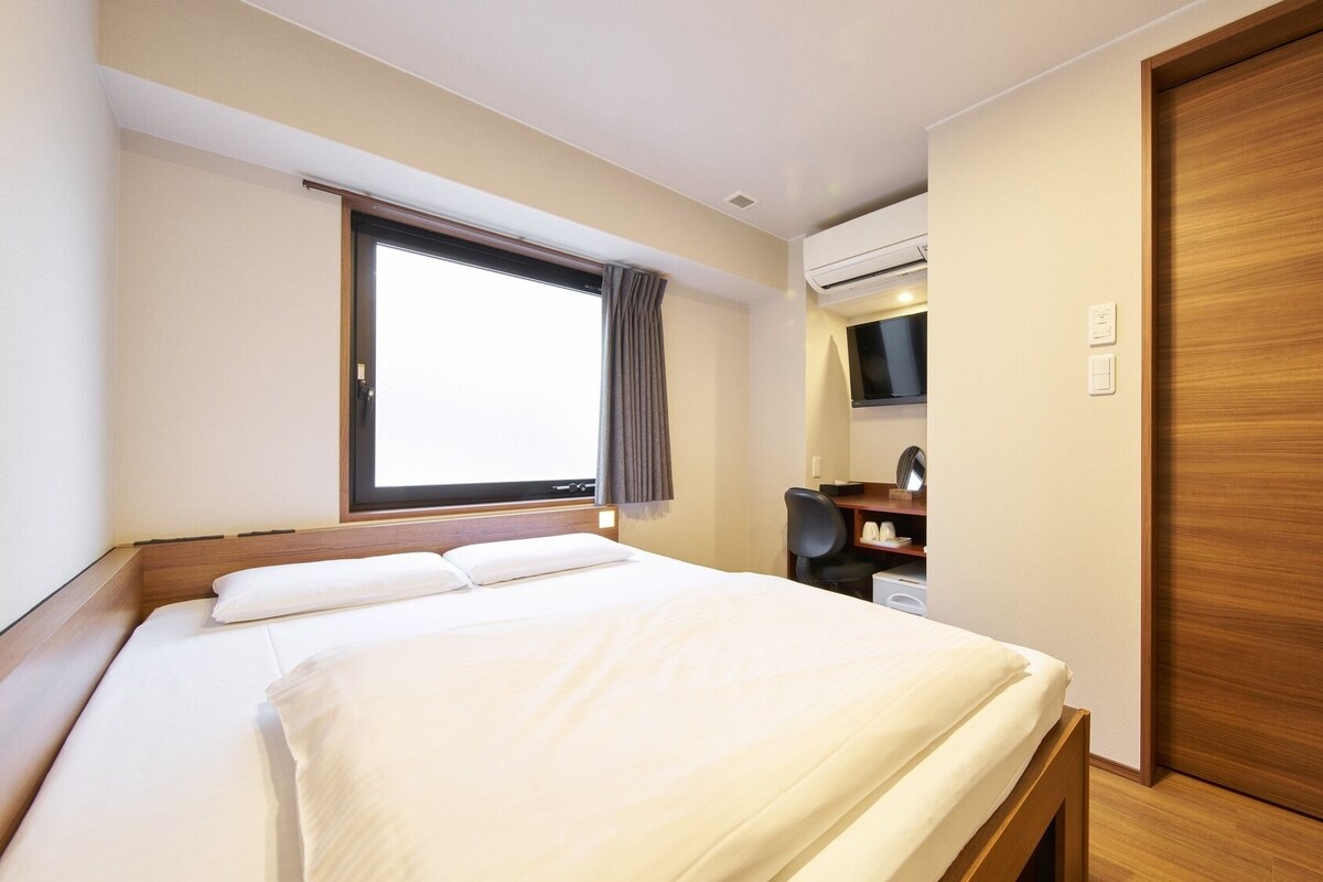 A hotel room with a bed, a desk, a TV, an air conditioning unit, and a wooden wardrobe.