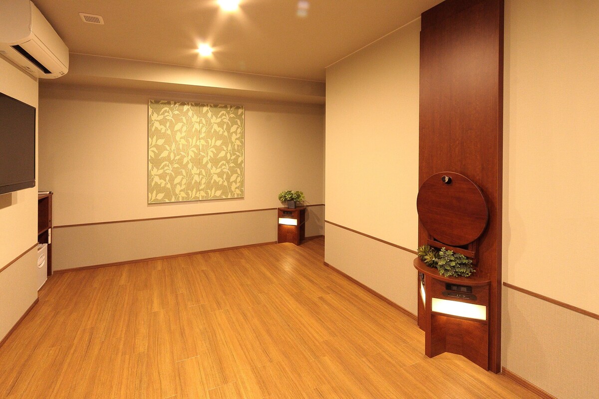 A room with wooden flooring, a window with a leaf pattern, a wooden door, and a small table with a plant.