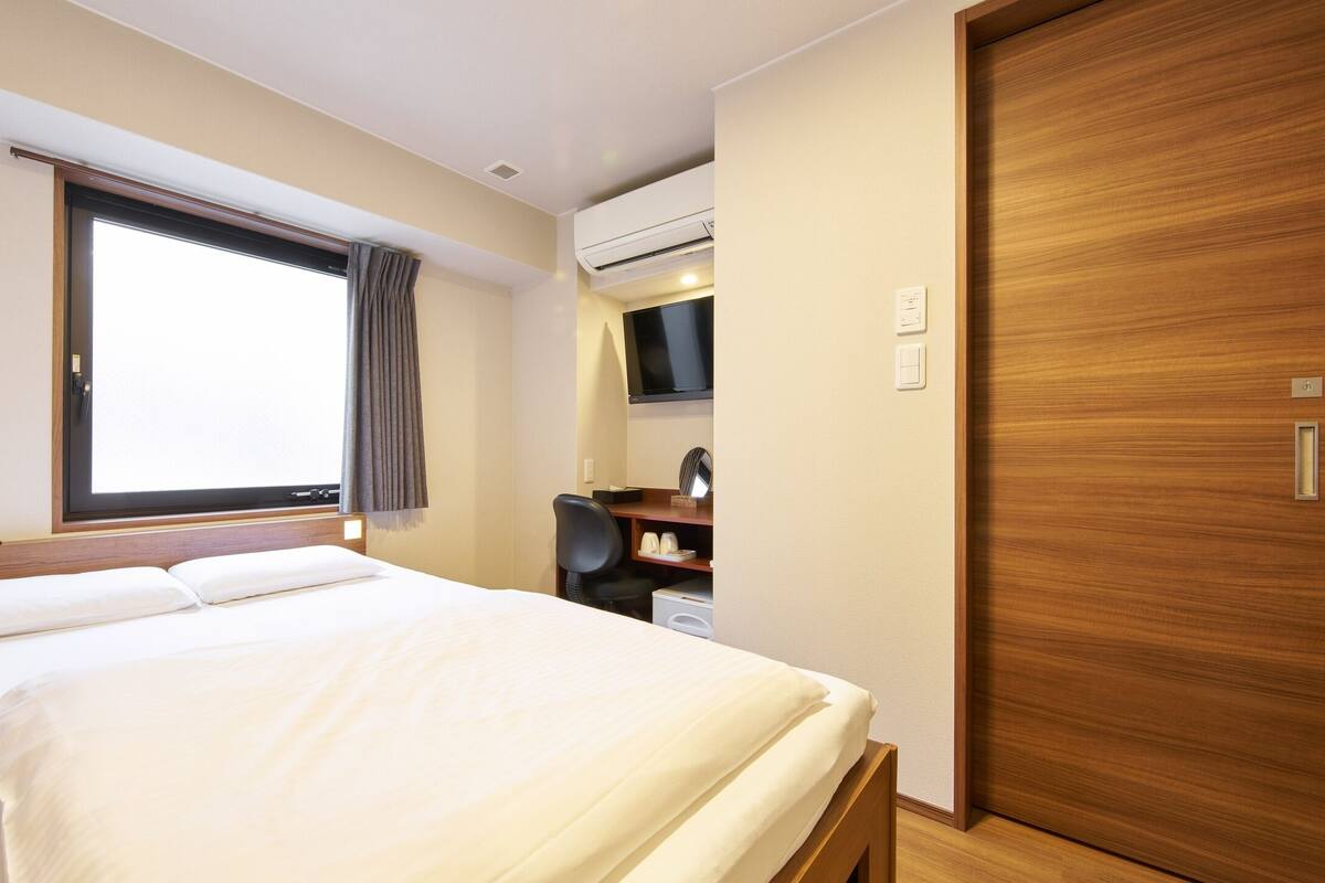 Habitación de hotel con cama, escritorio con silla, televisor y puerta de madera.