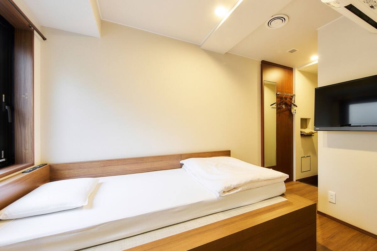 Una cama individual con cabecera de madera, un televisor de pantalla plana en la pared y una ventana con persianas.