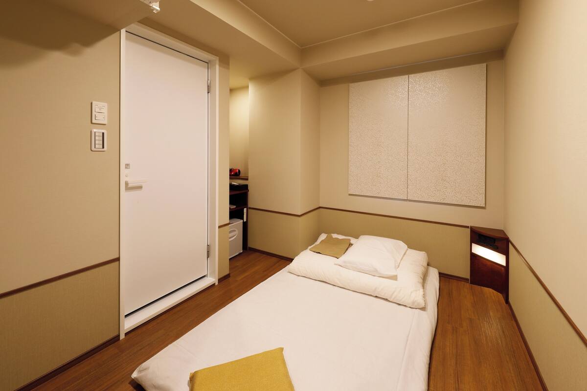 Una habitación de hotel con una cama, un armario, una mesita de noche y una lámpara fijada en la pared.