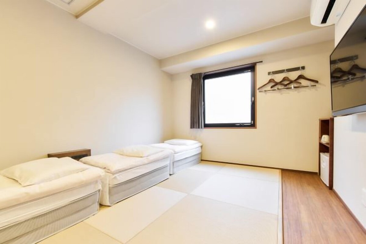 A room with two beds, a window, and a wall-mounted coat rack.