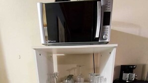 Uma bancada de cozinha com micro-ondas, copos e máquina de café.