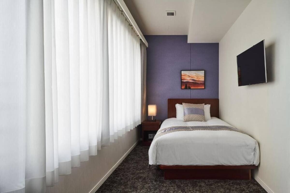 A hotel room with a large bed, a nightstand with a lamp, a painting on the wall, and a television on the wall.