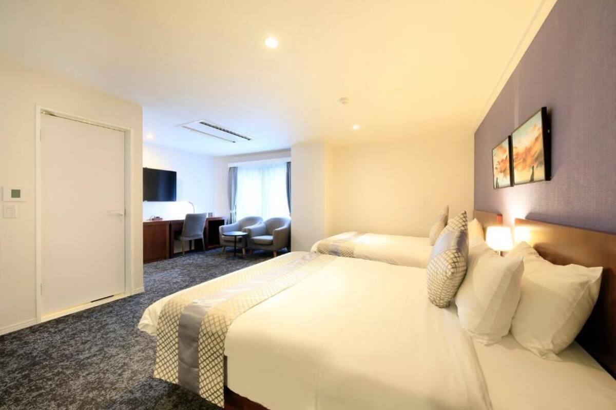 A hotel room with two beds, a desk, a chair, and a window with curtains.