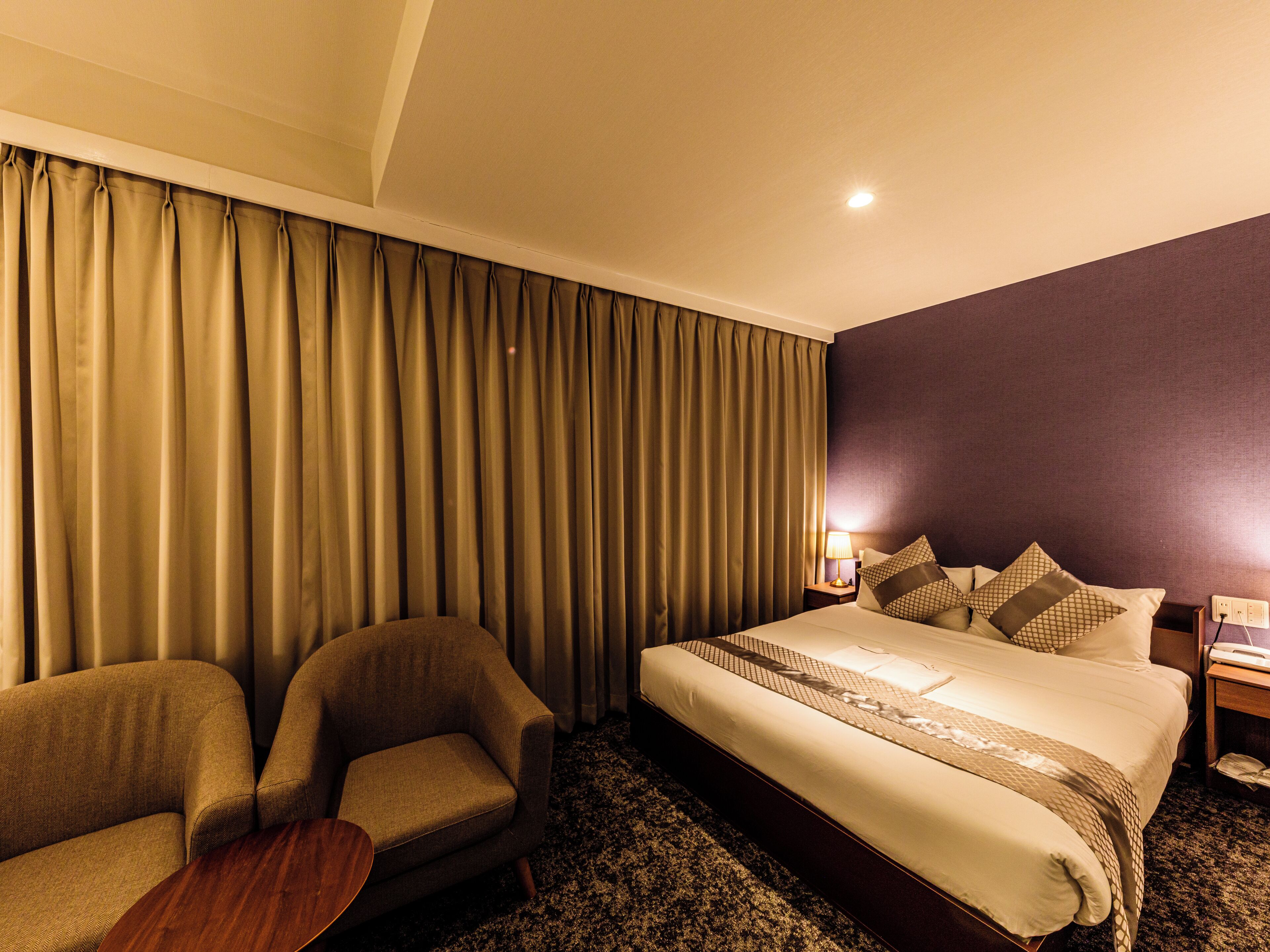 Une chambre d’hôtel avec un grand lit, deux fauteuils, une petite table et une table de chevet avec une lampe.
