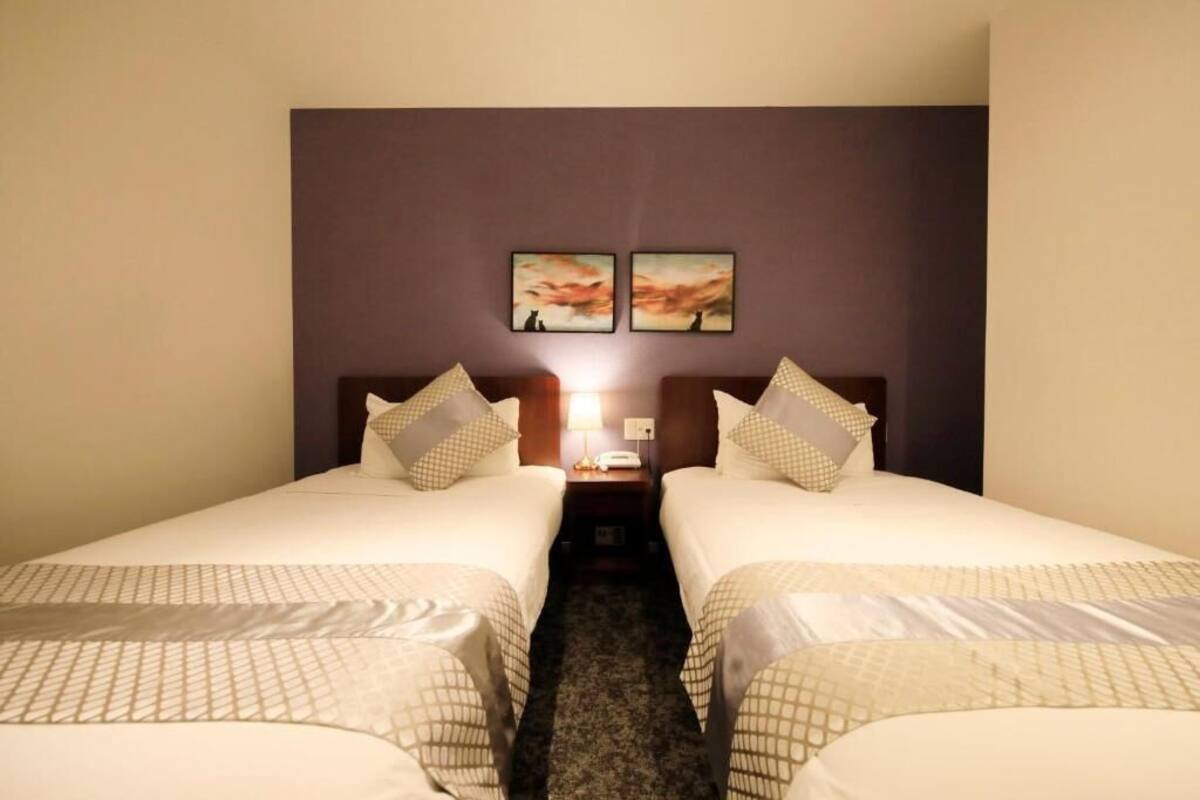 A hotel room with two single beds, a nightstand with a lamp, and two framed pictures on the wall.