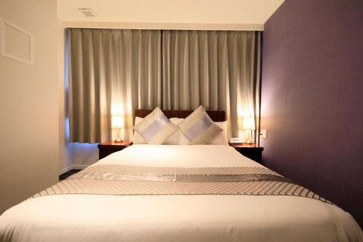 A hotel room with a large bed, two bedside tables with lamps, and a headboard with decorative pillows.