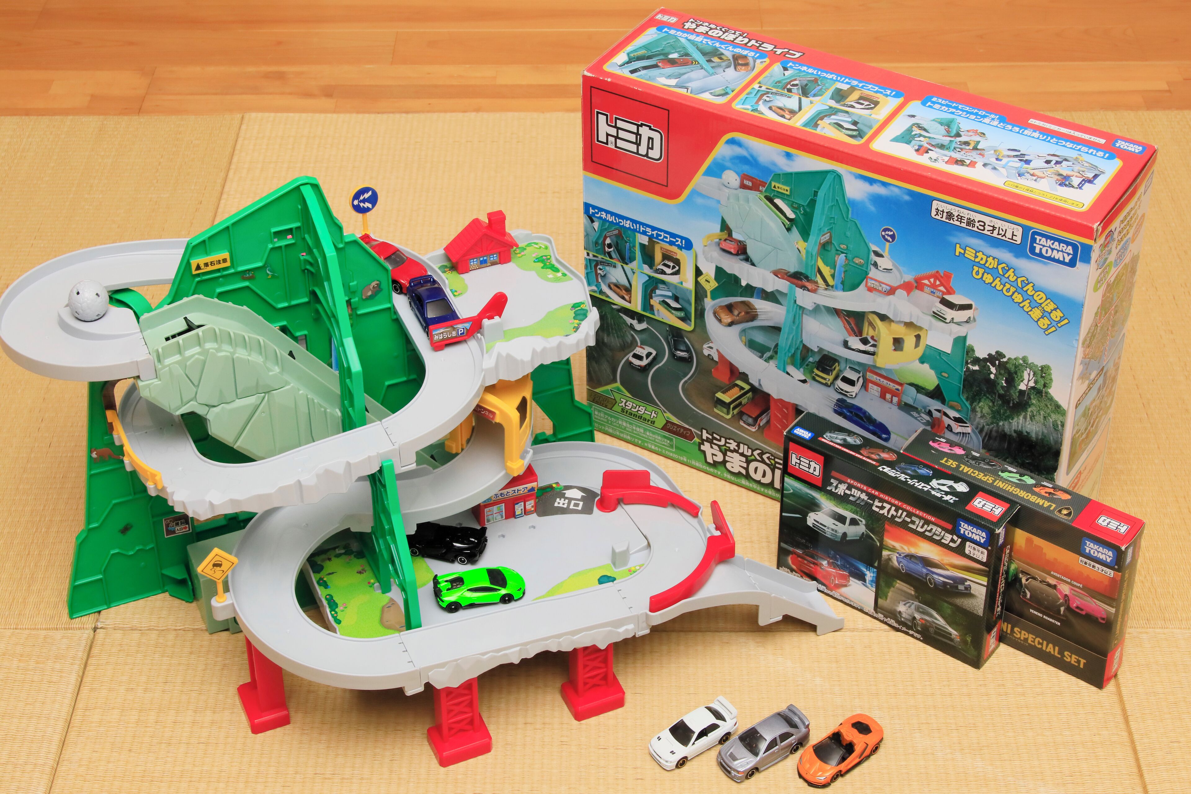 A toy car set with a green and white track, a box, and additional toy cars.