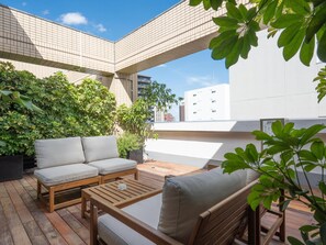 Un espace extérieur aménagé avec une table en bois et deux chaises rembourrées, entouré d’une végétation luxuriante et offrant une vue sur les bâtiments en arrière-plan.