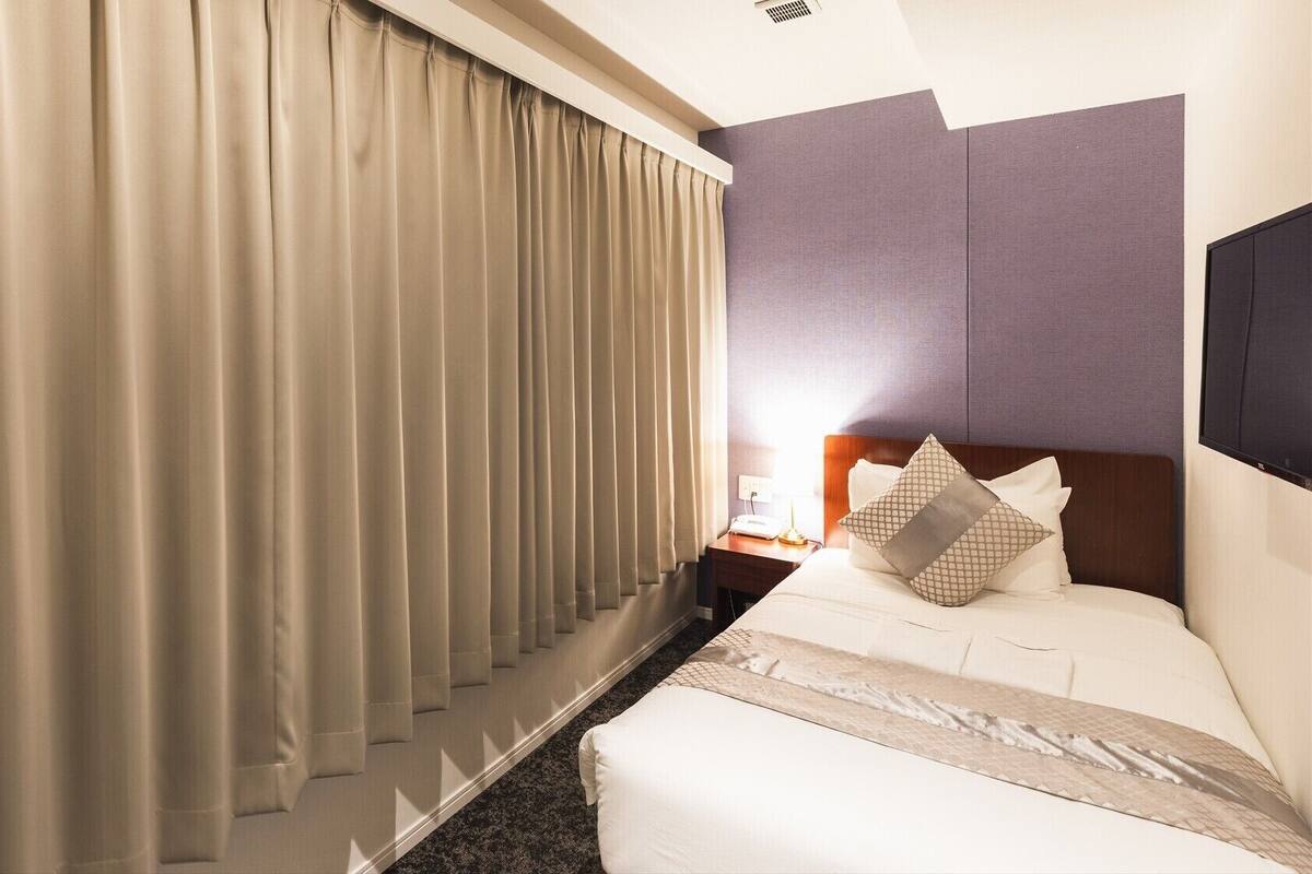 A hotel room with a bed, a nightstand, a lamp, and a window with curtains.