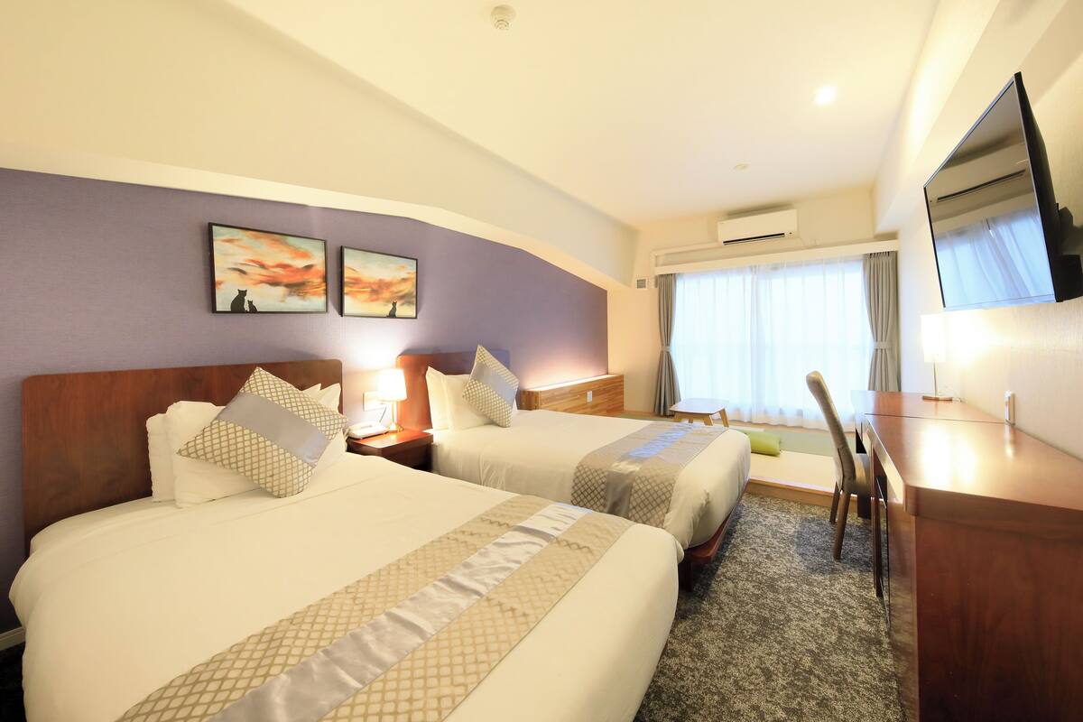A hotel room with two beds, a desk, a chair, and artwork on the wall.