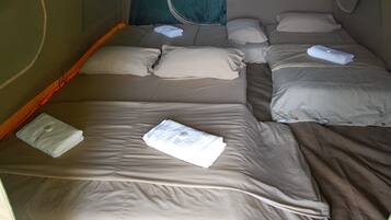 A single bed with beige bedding and pillows, a folded towel on the bed, and a window with curtains.