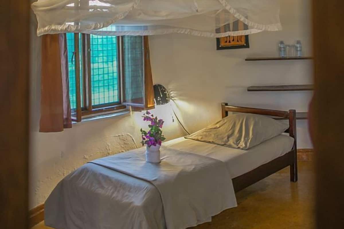 Una camera da letto con un letto, un comodino, una finestra con tende, una lampada da comodino e una mensola a parete.