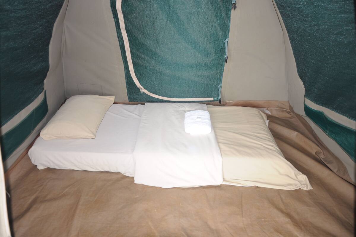 Una tenda con un letto all'interno, con materasso bianco e biancheria beige.