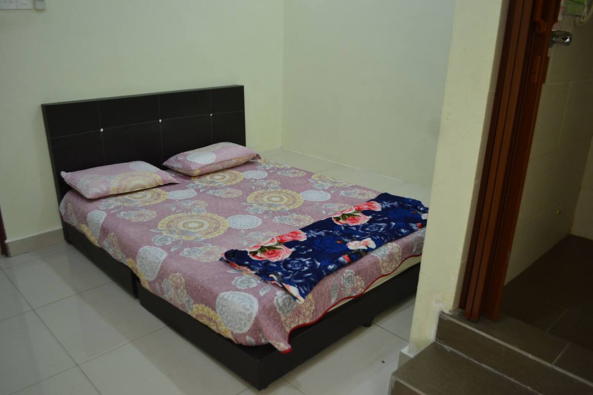 Una cama individual con una colcha estampada y dos almohadas, un cabecero oscuro y suelo de baldosas.