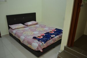 Uma cama de solteiro com um cobre-leito estampado e duas almofadas, uma cabeceira escura e piso de azulejos.