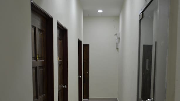 Un pasillo con piso de baldosas brillantes, puertas a la izquierda y una puerta de vidrio a la derecha.