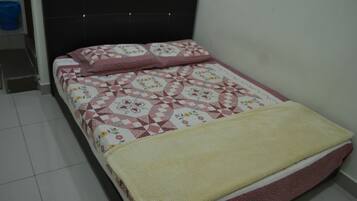 Una cama con una colcha estampada y una manta amarilla, un cabecero oscuro y una pared blanca.