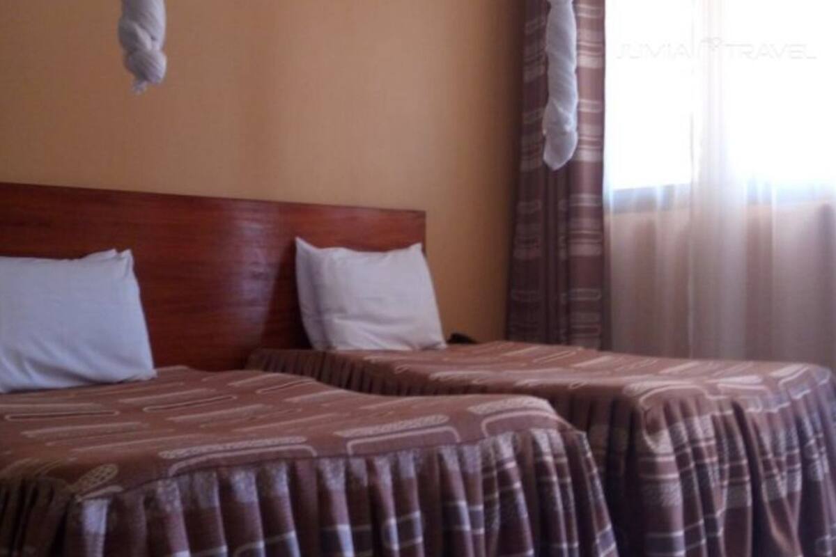 A hotel room with two beds, each with a patterned bedspread and white pillows.