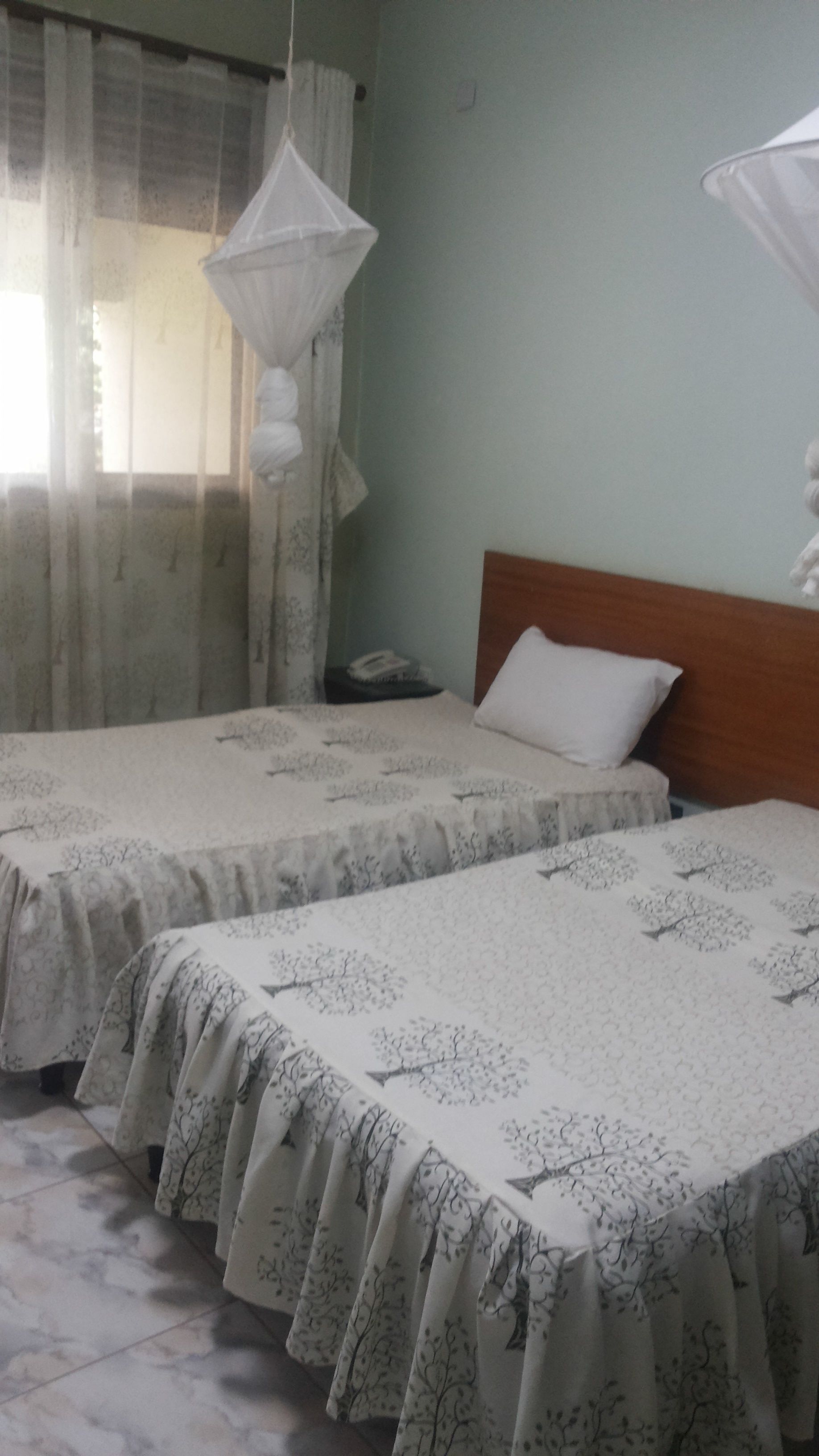 A bedroom with two beds, each with a patterned bedspread and a white pillow. There is a wooden headboard on one bed, and a small bedside table with a lamp.